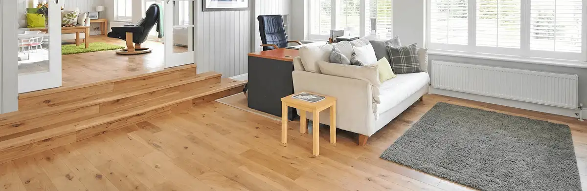 A modern living room with professionally installed laminate flooring, a beige sofa, a small side table, a gray rug, and large windows with white shutters in Detroit, MI